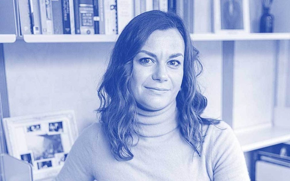 A woman seated in front of a bookshelf filled with various books, engaged in reading or contemplation.