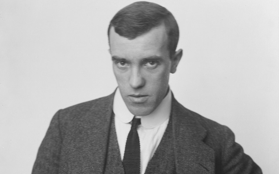 A black and white photograph of a man in a three-piece suit standing with hands on hips.