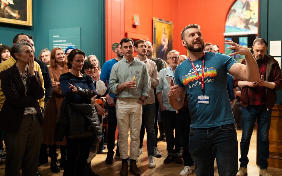 Photograph of a group tour led by a man pointing at a painting off to the right