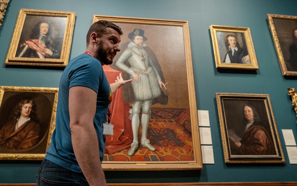 Man giving a tour pointing at a large oil painting.