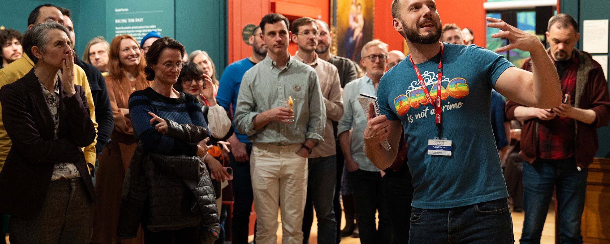 Photograph of a group tour led by a man pointing at a painting off to the right