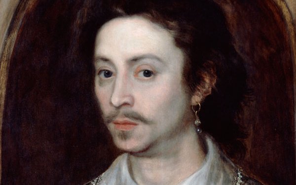Portrait of a man wearing a white silk shirt with intricate black patterns. He has shoulder length dark hair and wears a hanging pearl earring in his left ear.