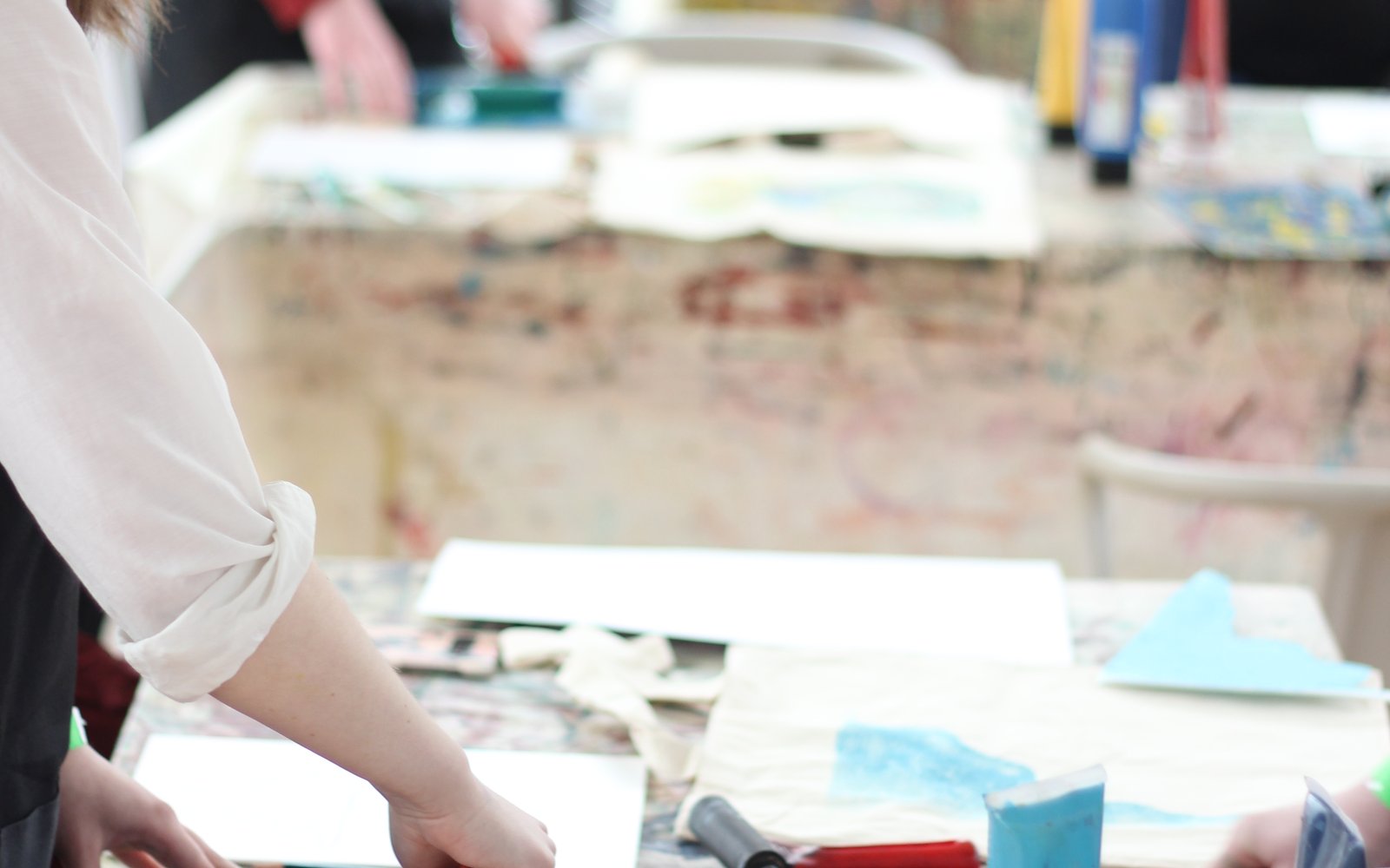 Two young people stand at a table painting with art supplies around the table.