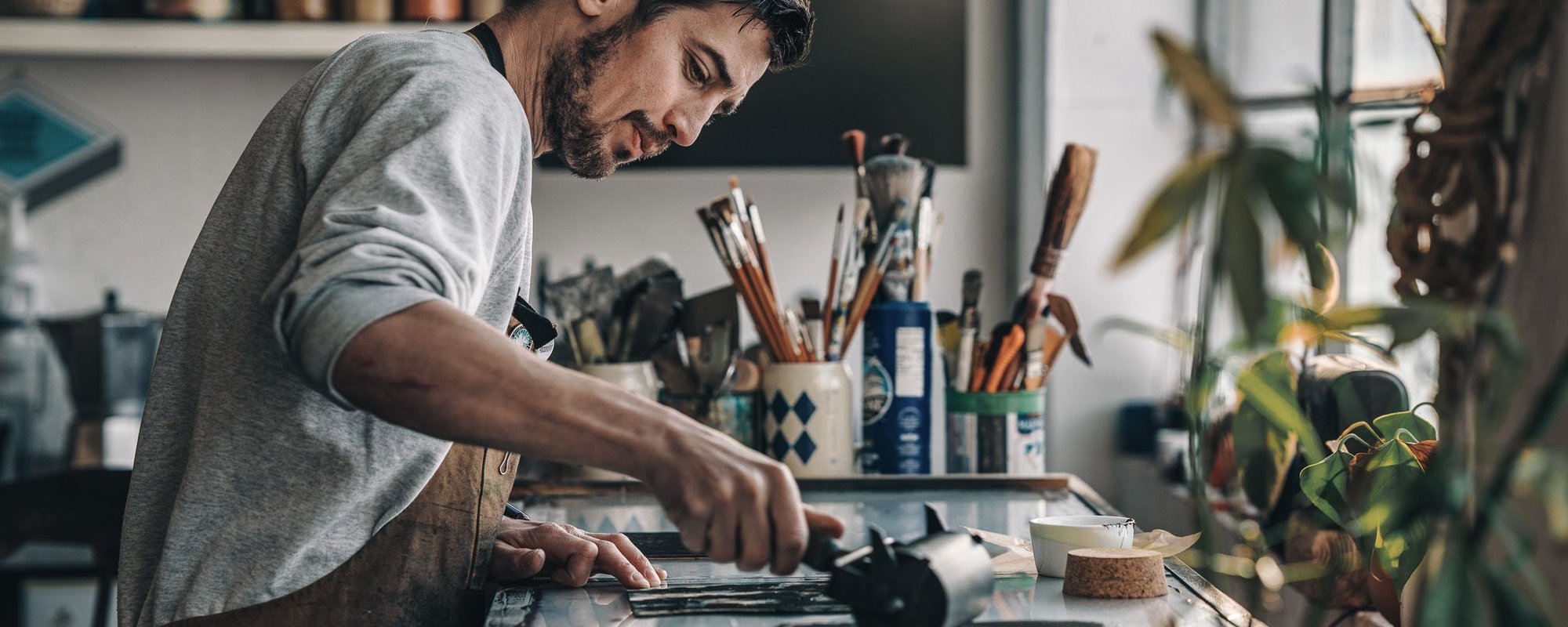 Alex Booker creates art in his studio, surrounded by various tools and materials, focused on his work.