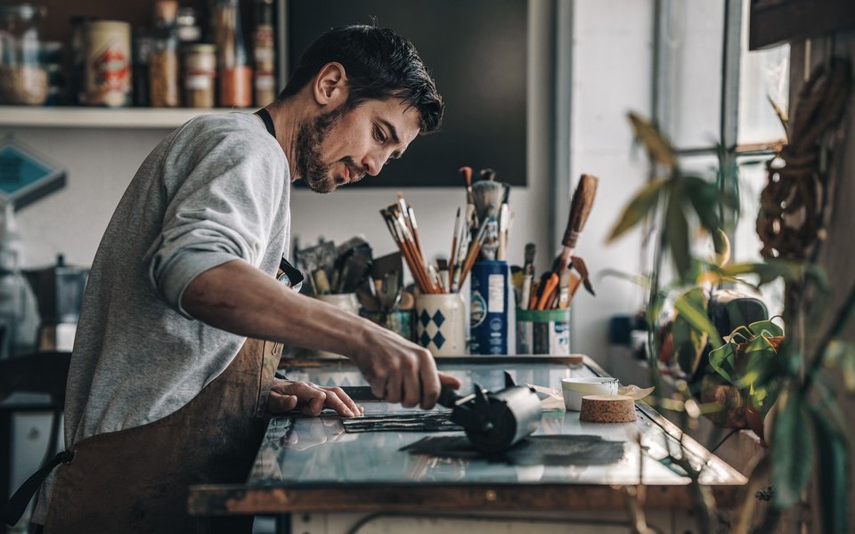Alex Booker creates art in his studio, surrounded by various tools and materials, focused on his work.