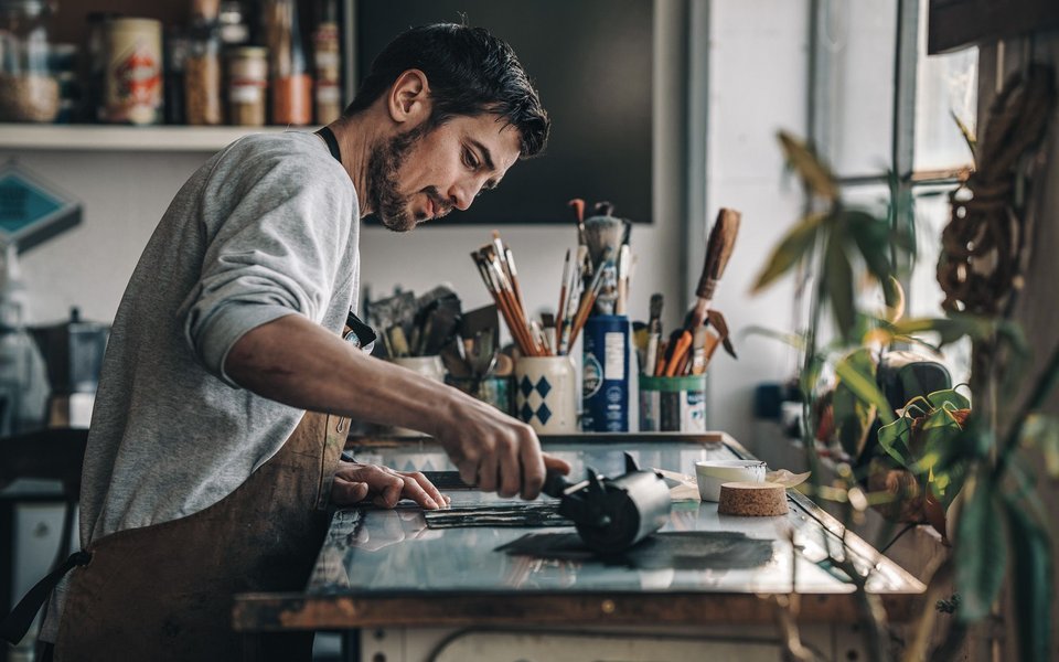 Alex Booker creates art in his studio, surrounded by various tools and materials, focused on his work.