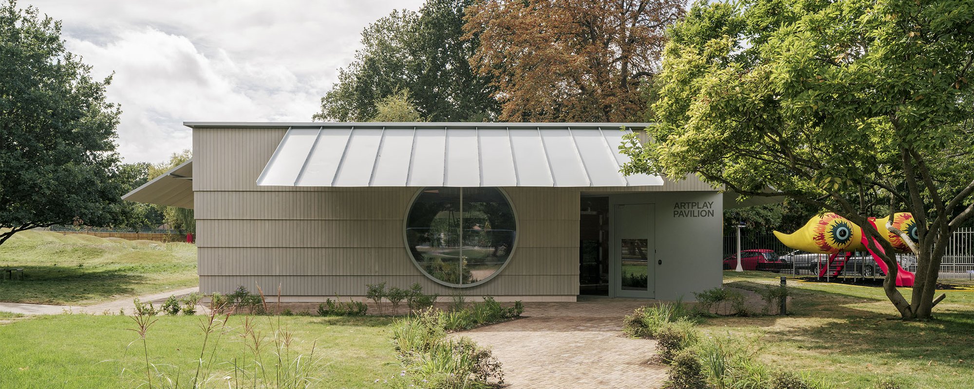 A wood paneled building with a large circular window in a garden setting.
