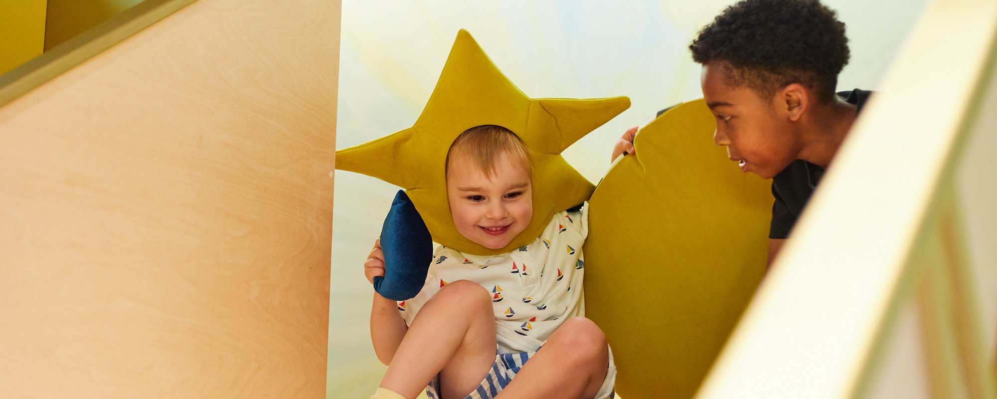 Two children at the top of a slide. One on left wears a star hat.