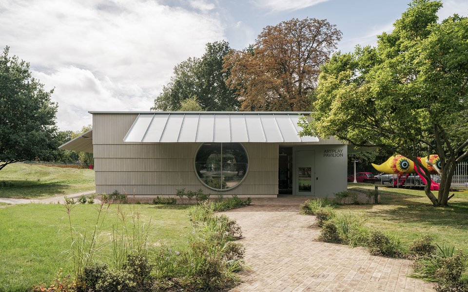 A wood paneled building with a large circular window in a garden setting.