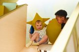 Two children at the top of a slide. One on left wears a star hat.