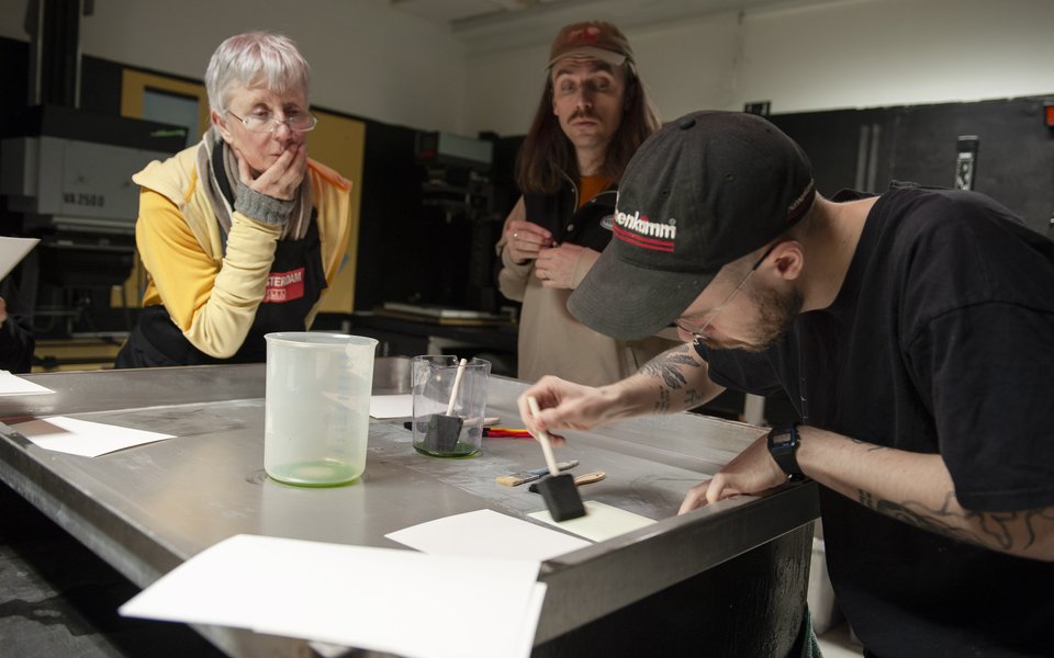 A man paints a chemical on a piece of paper while two others look on