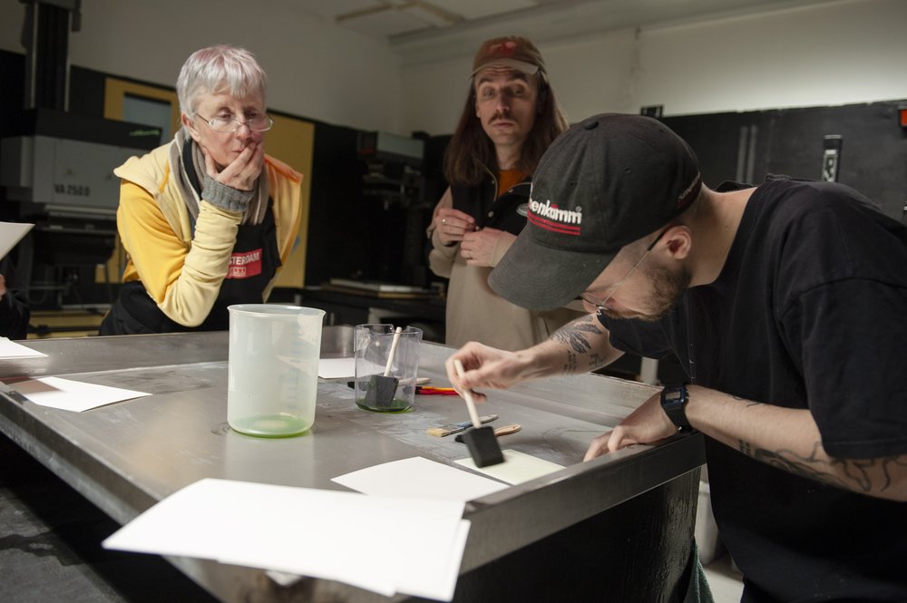 A man paints a chemical on a piece of paper while two others look on
