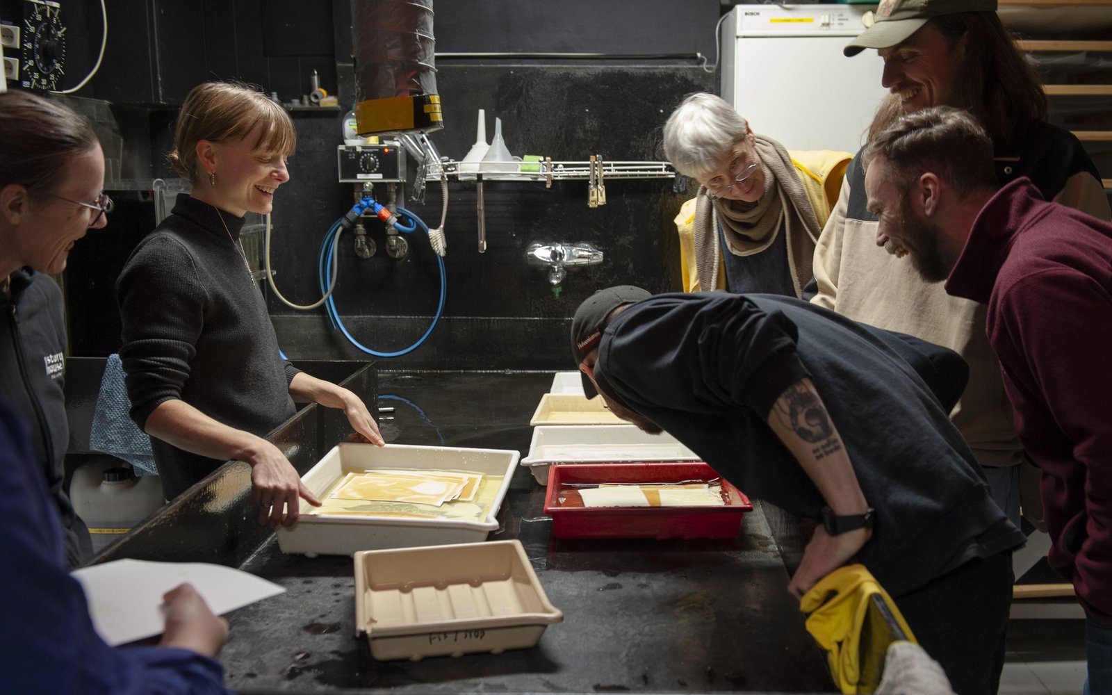 Trays of developing prints on a table with people around looking in