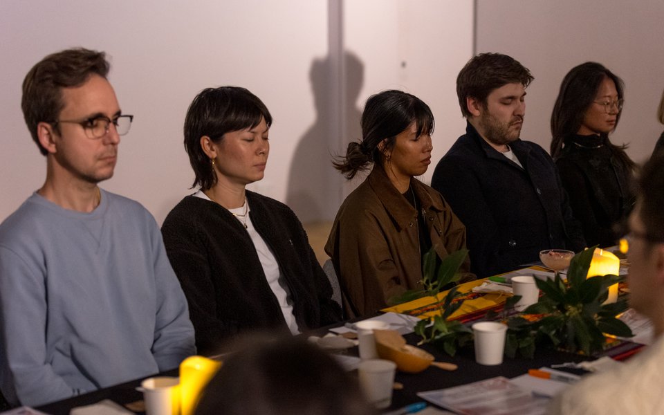 5 people sat in a row at a table with their eyes closed.