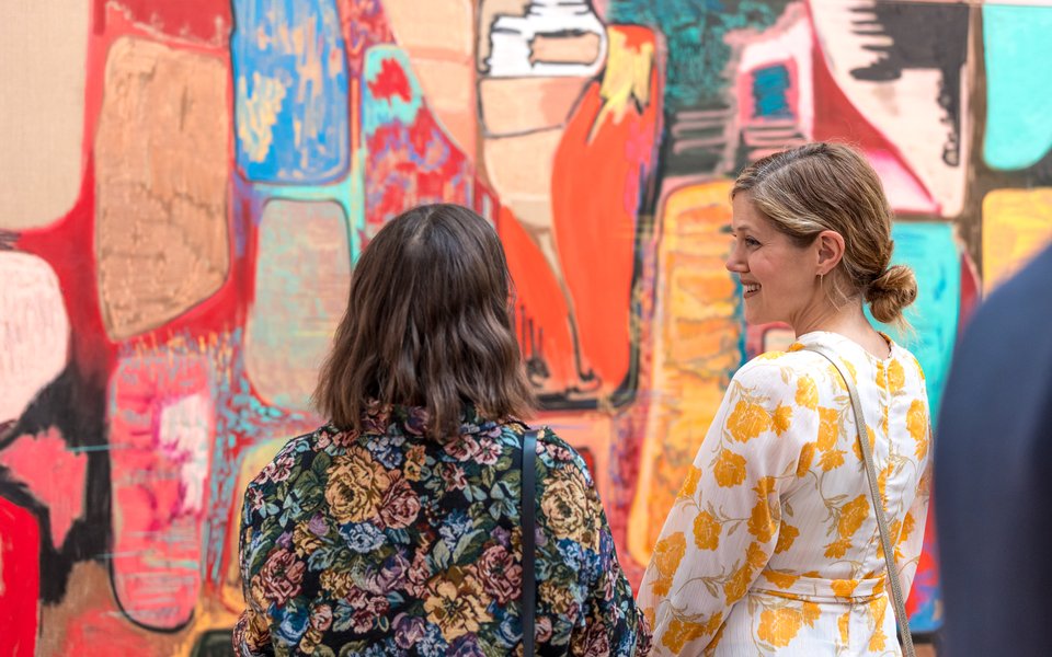 Two women stand talking in front of large abstract painting by Rachel Jones