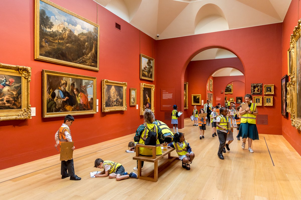 A school group with children wearing yellow or orange high vis vests exploring the main gallery.