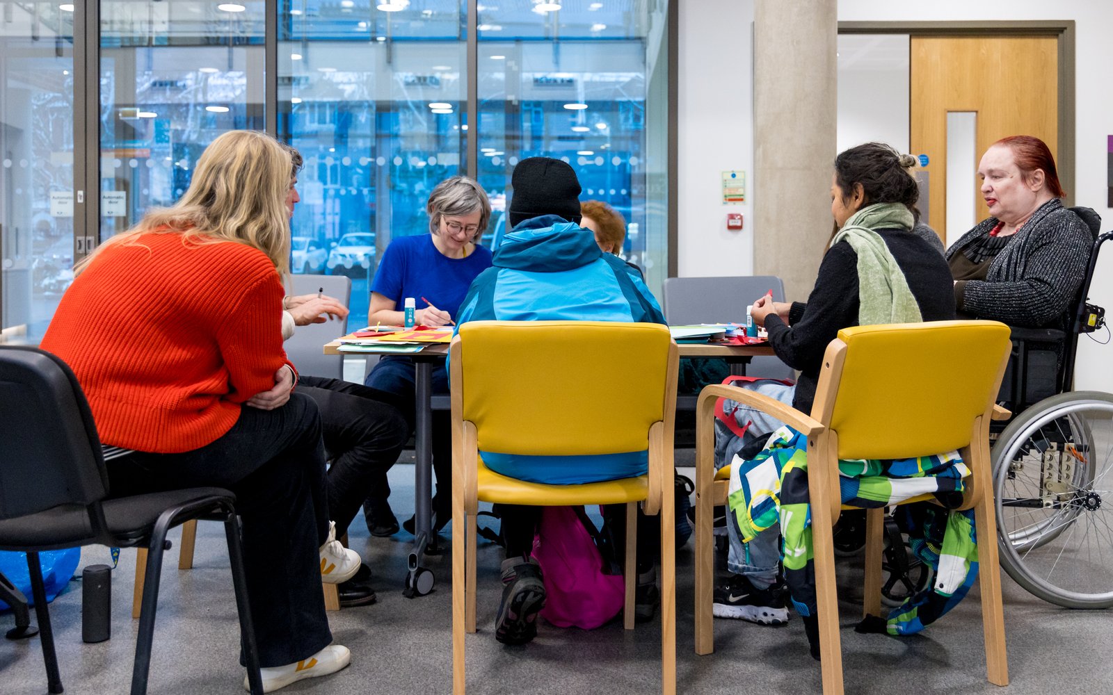 A group sat at a table chatting and crafting. Photo taken from behind.