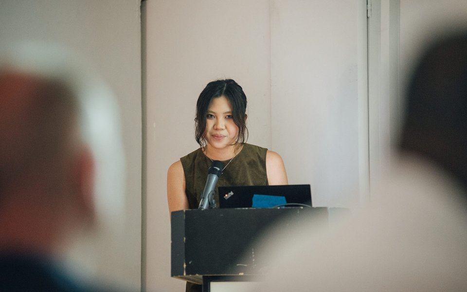 A woman gives a presentation from a lectern to an audience sat in front
