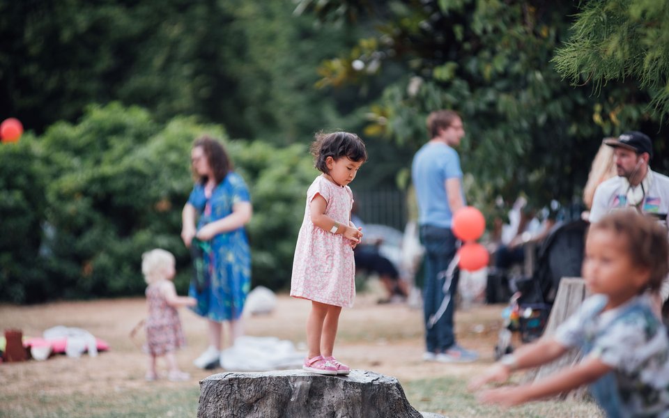 Children play in a garden with focus on a young girl stood on a bronze tree stump.