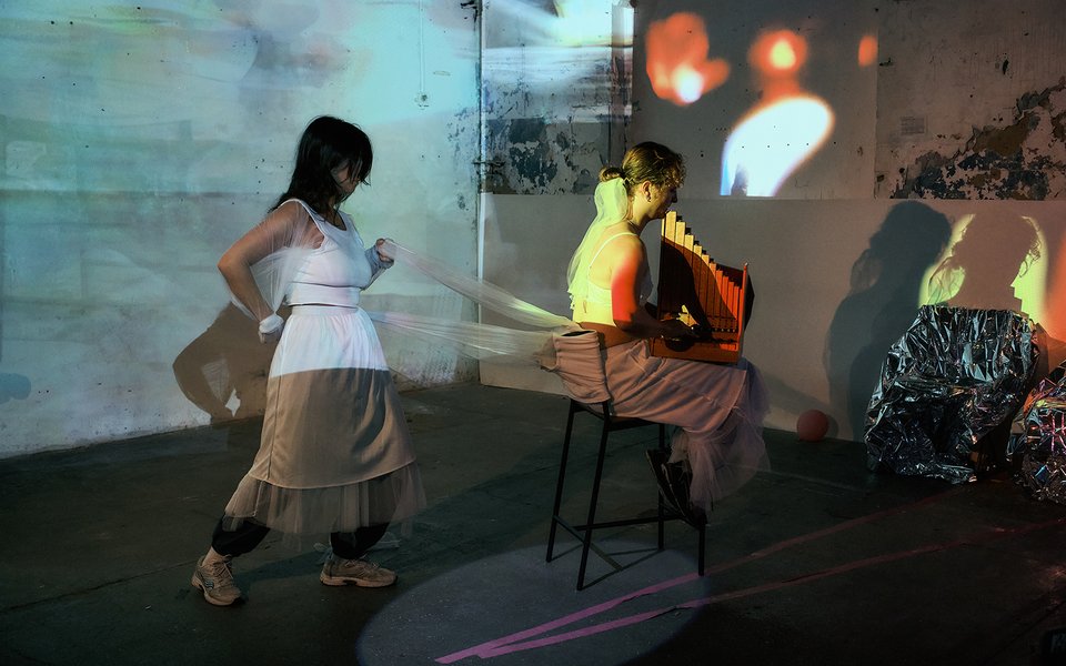 Live performance with a person sat in a chair being pulled backwards by a person standing behind via some material