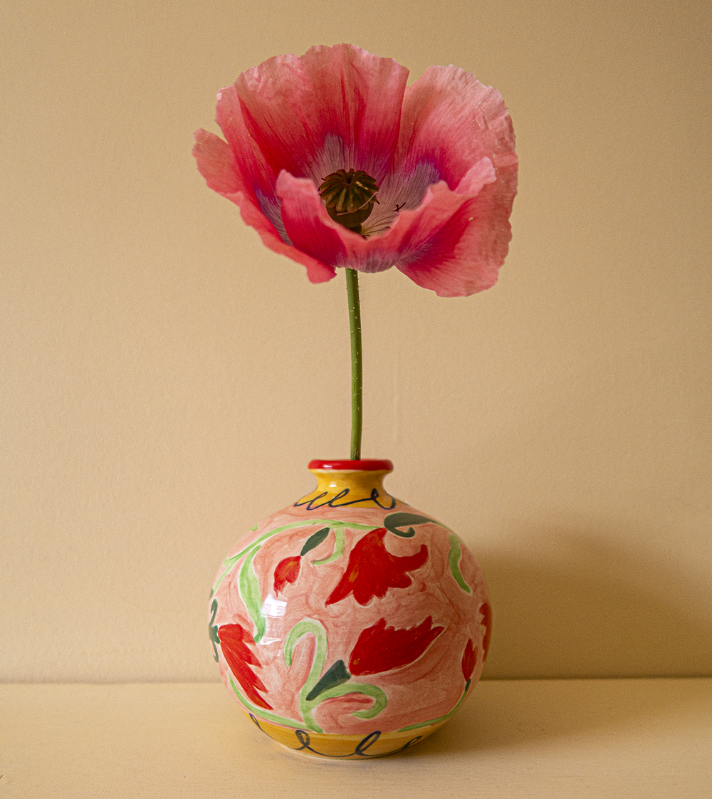 A brightly coloured orange and pink vase with a pink flower in it