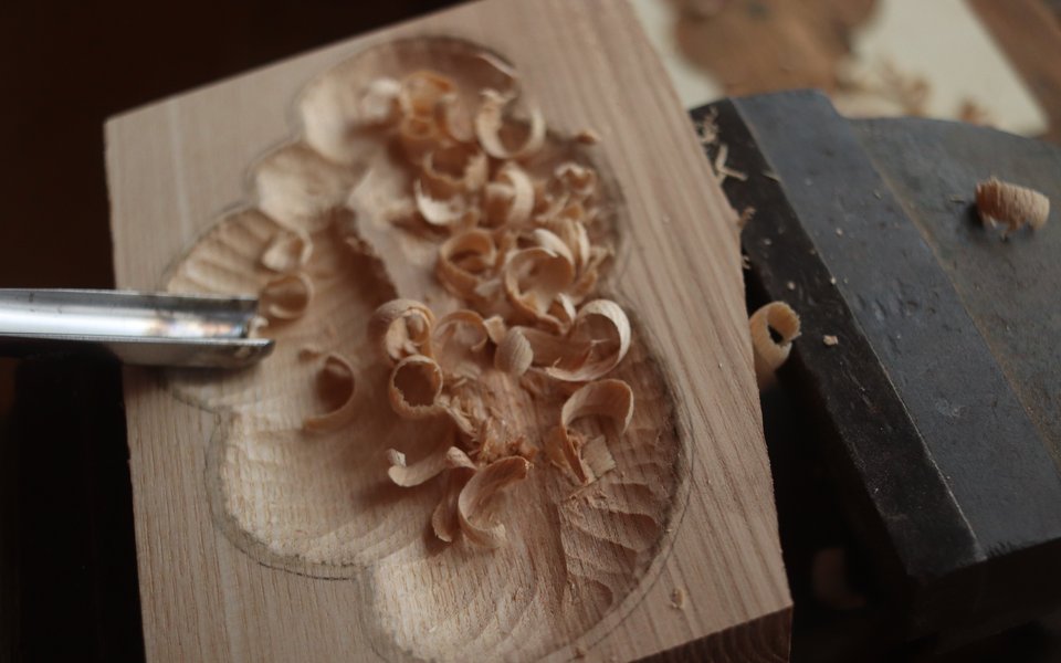 A hand carving wood with a metal tool.