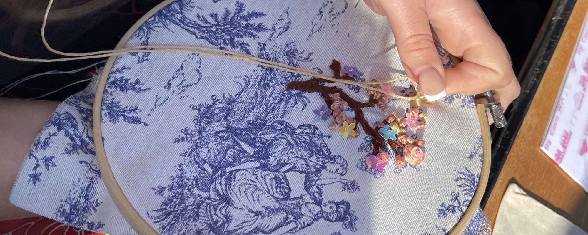 Close up of someone embroidering a landscape scene with a large tree.