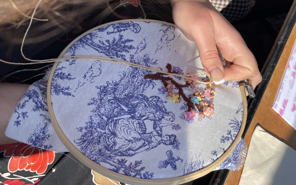 Close up of someone embroidering a landscape scene with a large tree.