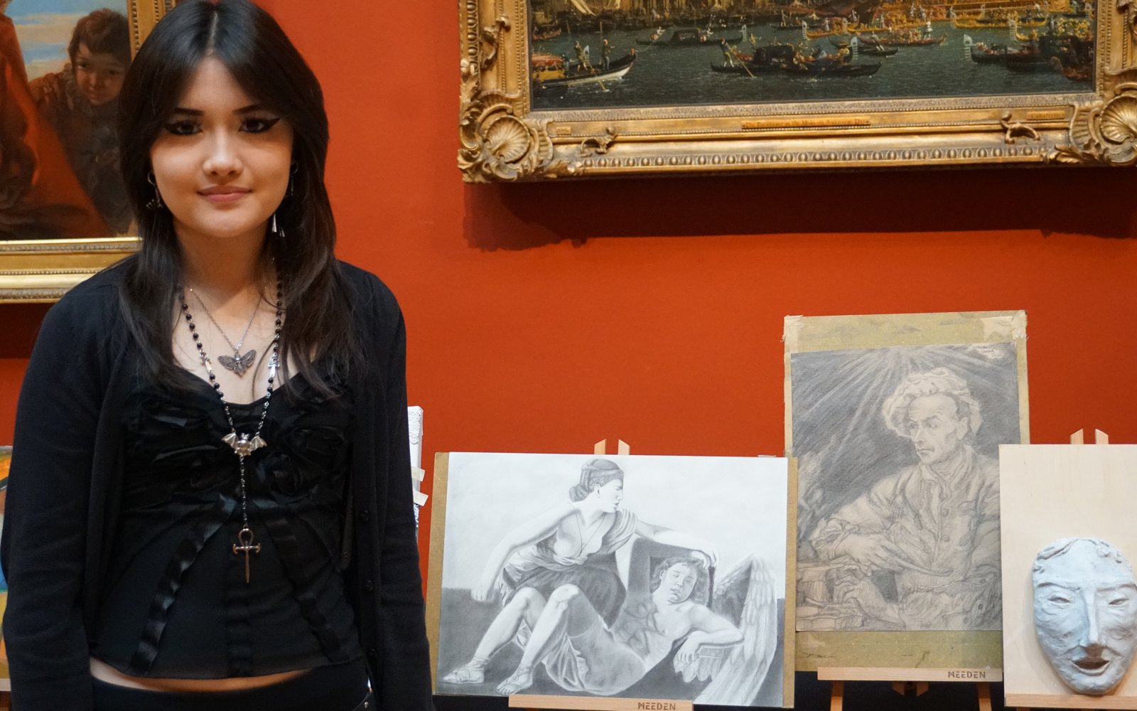 Young girl with long dark hair stood next to a display of sketches