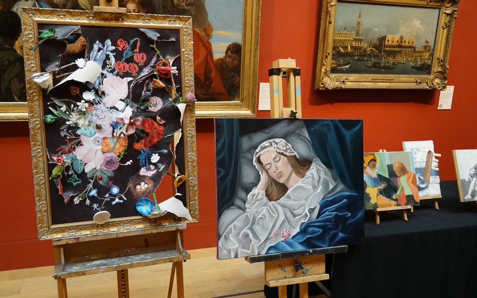 Paintings on easels next to a table in a gallery space
