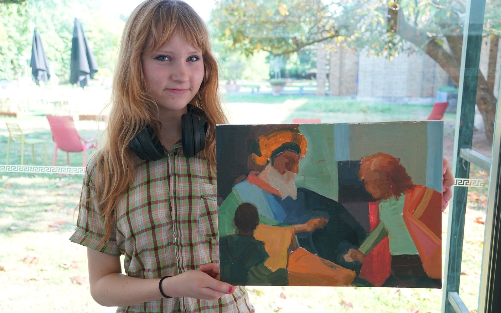 A young woman with stood in front of a window holding a painting