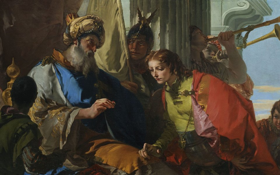 A man in a robe and turban hands a ring to a young man right who bends to look at it.