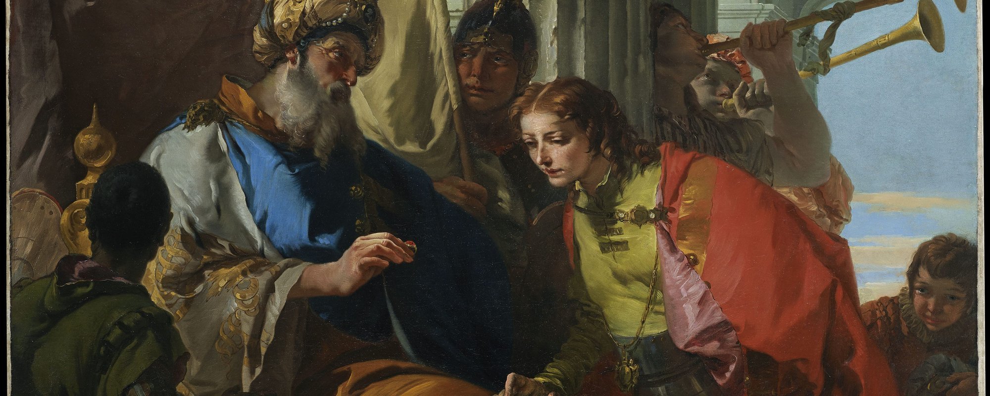 A man in a robe and turban hands a ring to a young man right who bends to look at it.