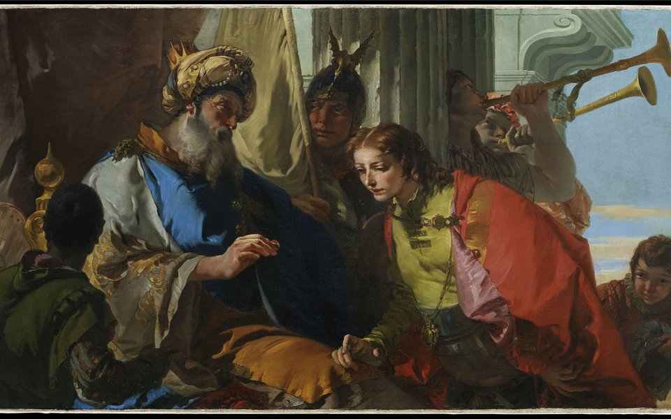 A man in a robe and turban hands a ring to a young man right who bends to look at it.