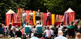 A play on an outdoor stage with 4 actors acting with a crowd sat in front.