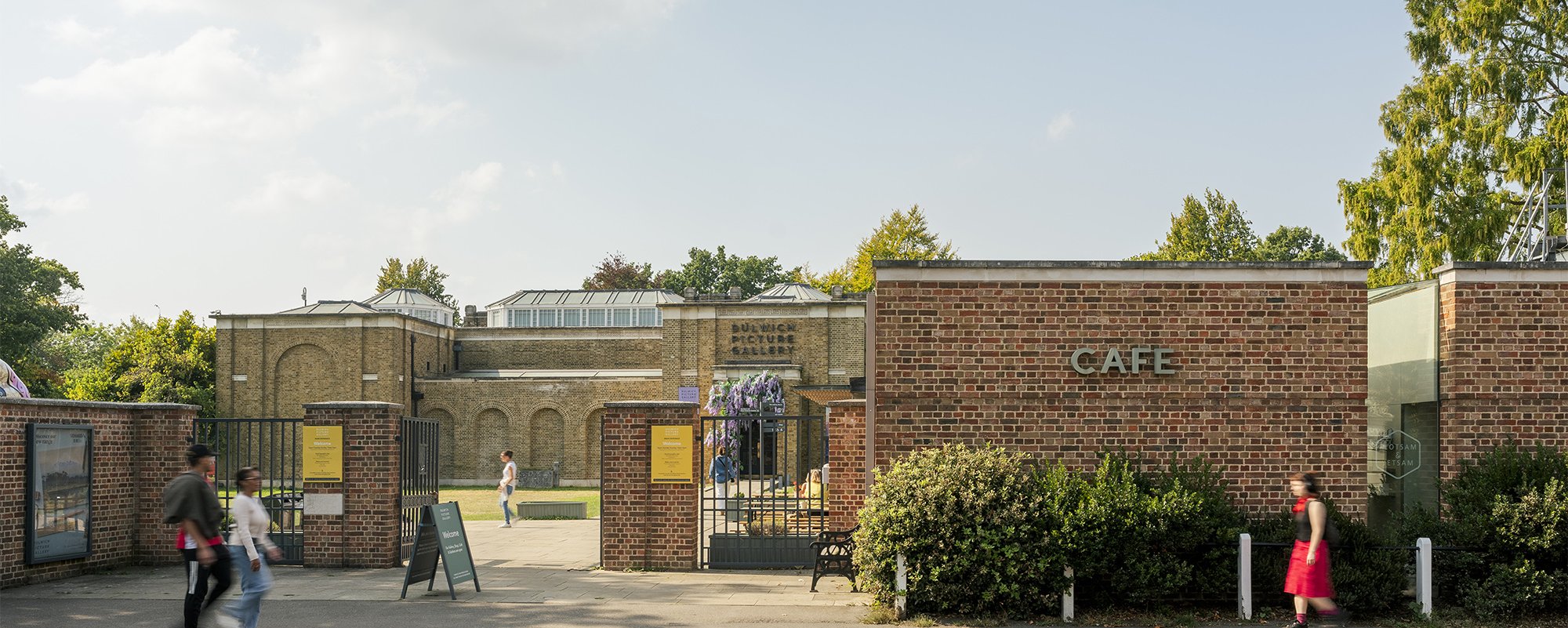 Dulwich Picture Gallery entrance with cafe to right and gate to left with Gallery buildings just visible behind gate.