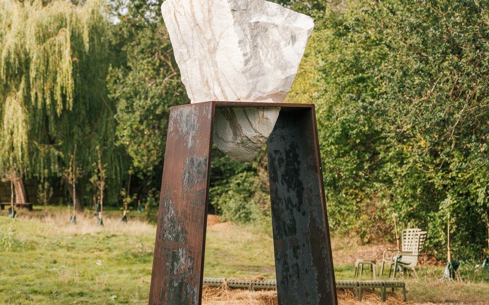 A large abstract sculpture stands prominently in a green field under a clear blue sky.