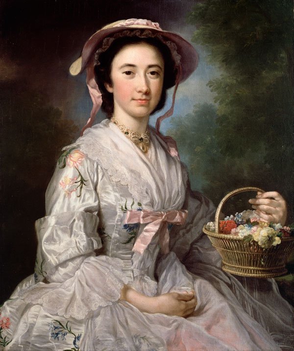 Portrait of a woman in a straw hat and white floral dress carrying a basket with flowers.