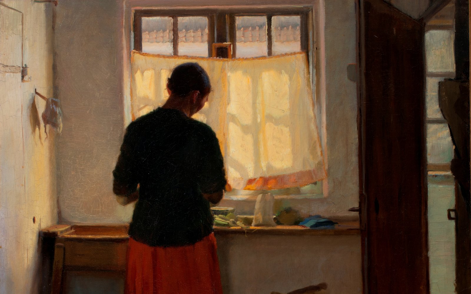 A woman stands at a sink with her back to viewer in a kitchen