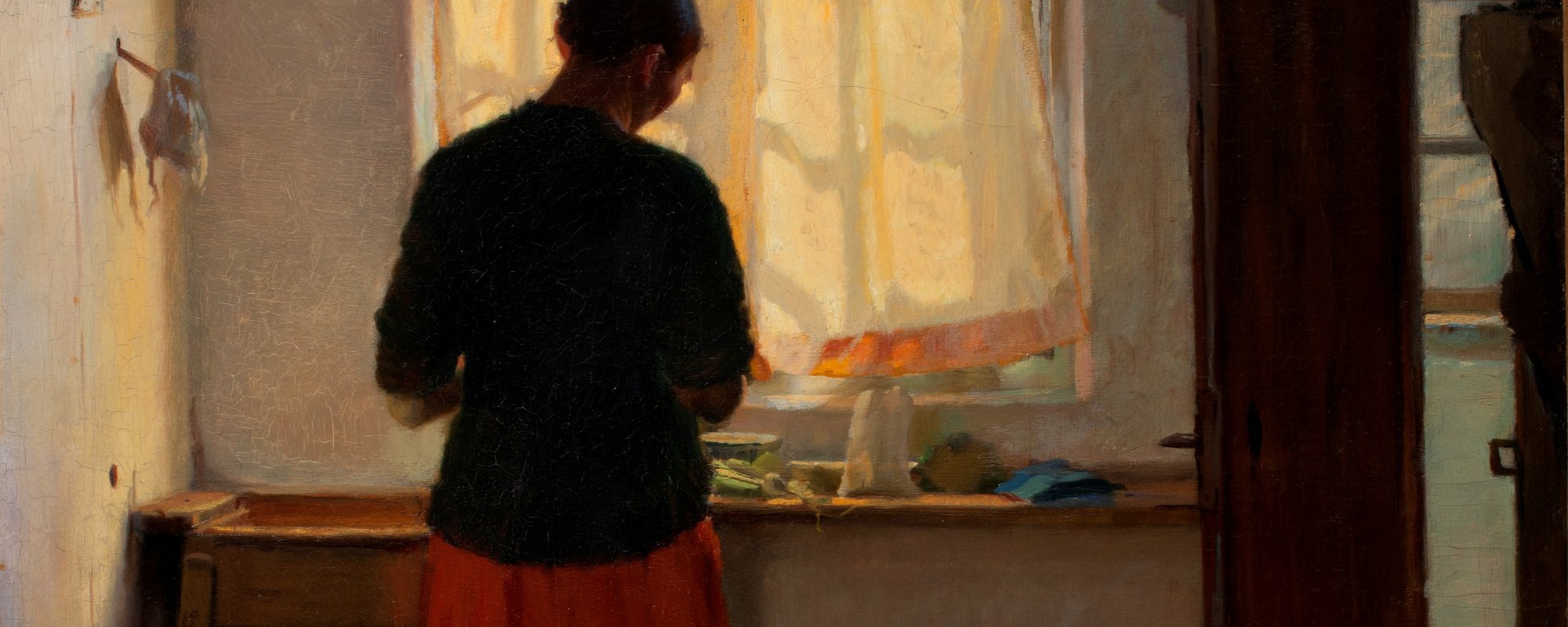 A woman stands at a sink with her back to viewer in a kitchen