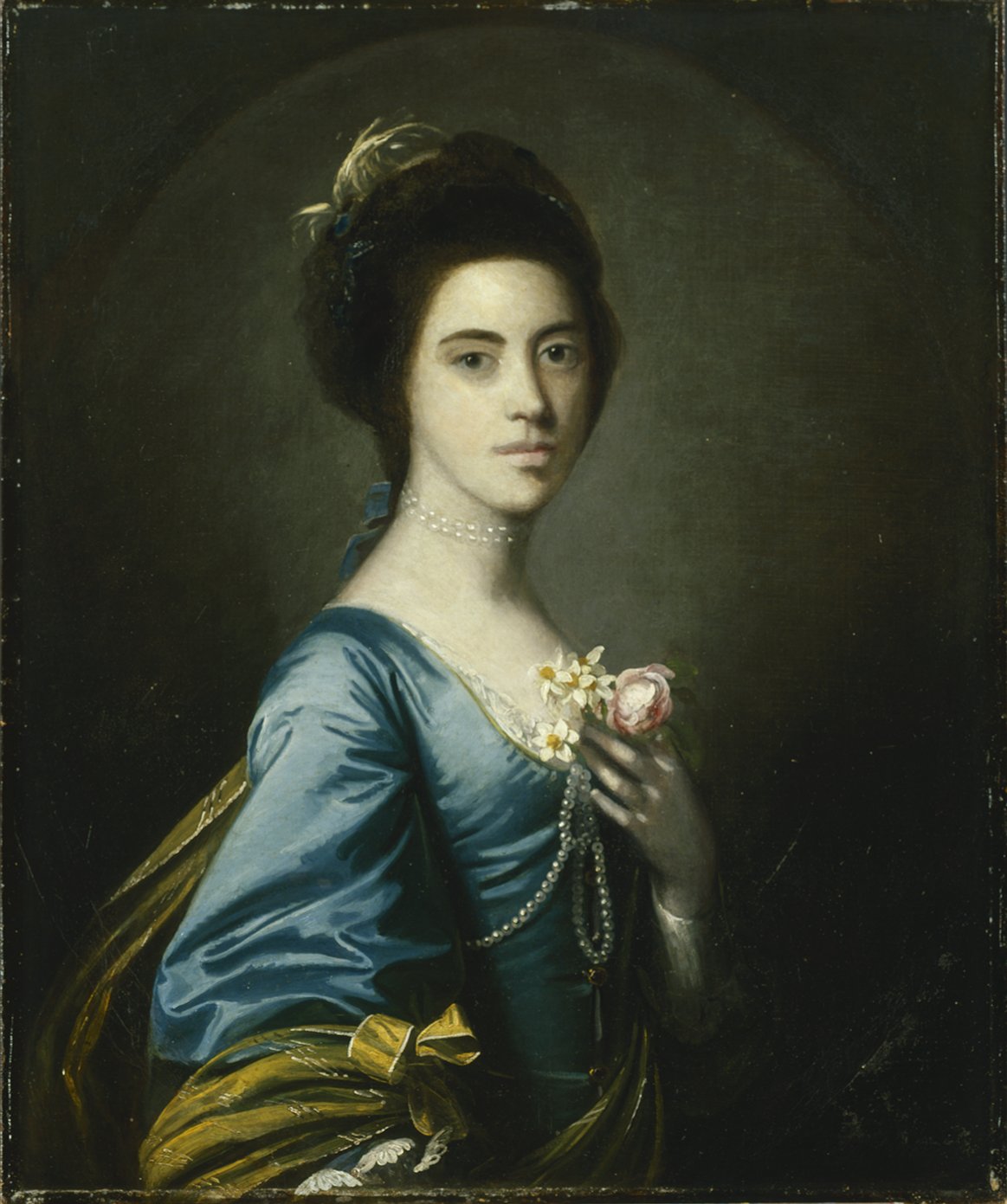 Portrait of a woman in a blue dress with dark hair holding a flower at her breast.