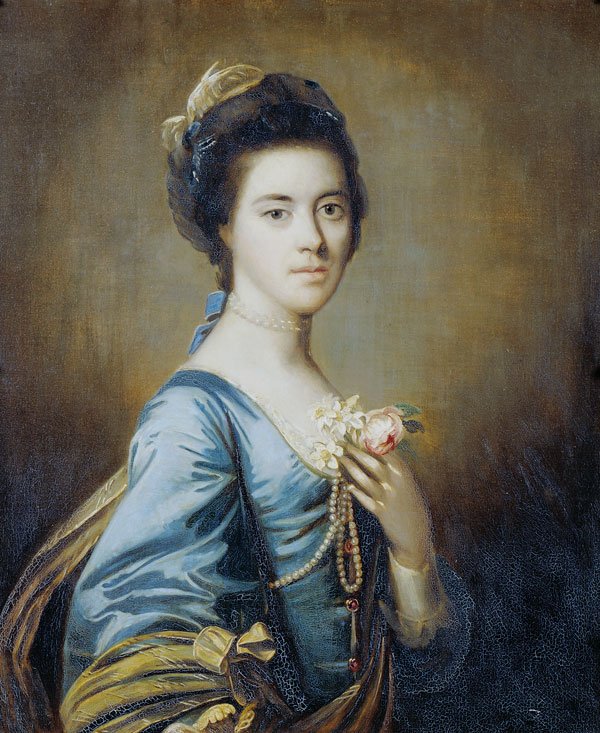 Portrait of a woman in a blue dress with dark hair tied on head. She holds her left hand to her breast with pearls and a rose. The background is brown.