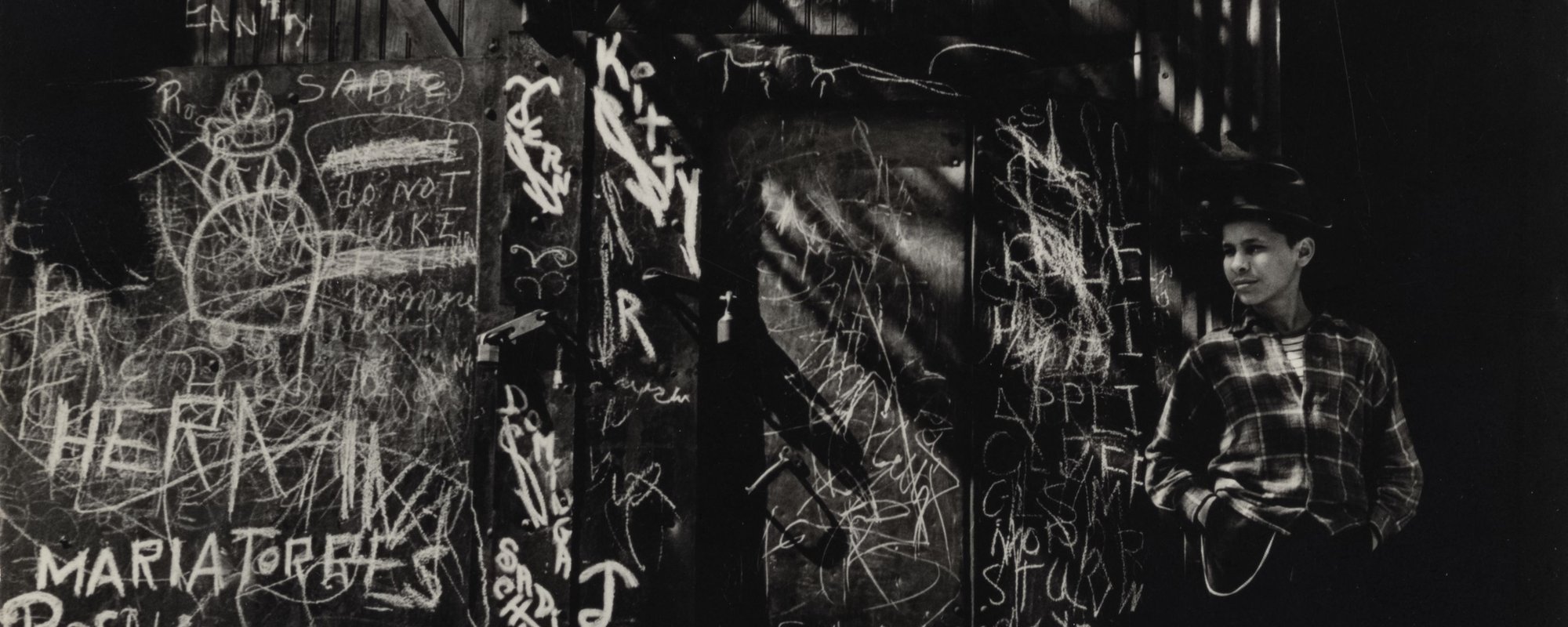A child leaning against a graffiti wall under a metal staircase