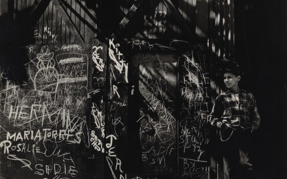 A child leaning against a graffiti wall under a metal staircase