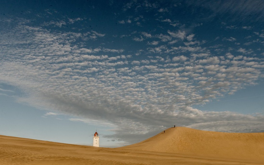 Sand dunes with top of lighthouse poking up from behind.