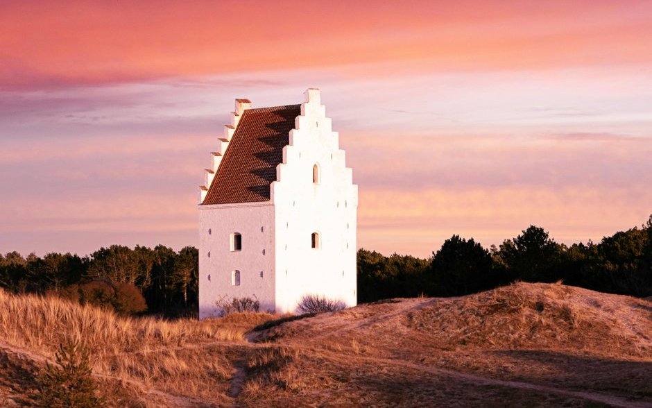 A white church tower with crenelated peak on a sand dune