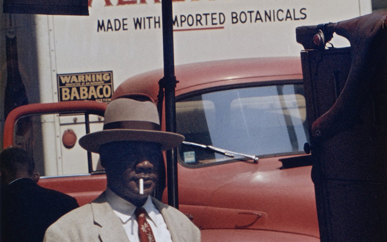A man in a hat and suit walking underneath a sign saying House with a smaller sign saying bar underneath.