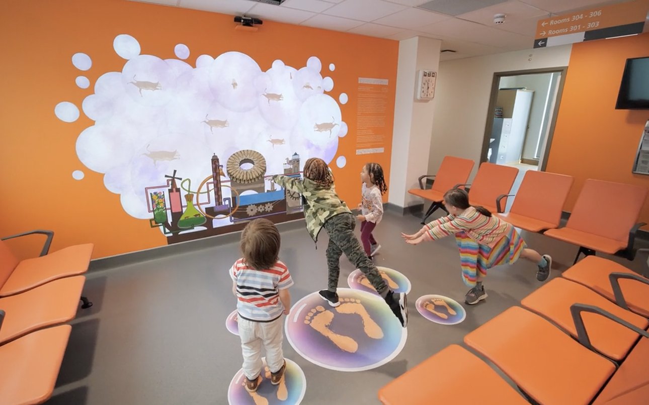 Children play with an interactive artwork in a bright orange room