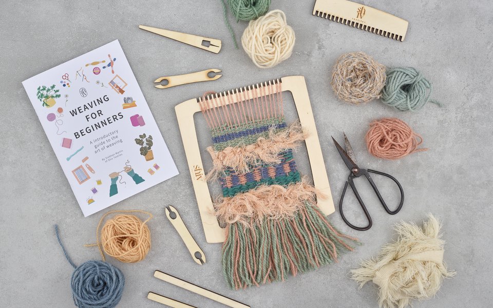 A weaving kit featuring scissors, colorful yarn, and additional crafting tools arranged neatly on a table.