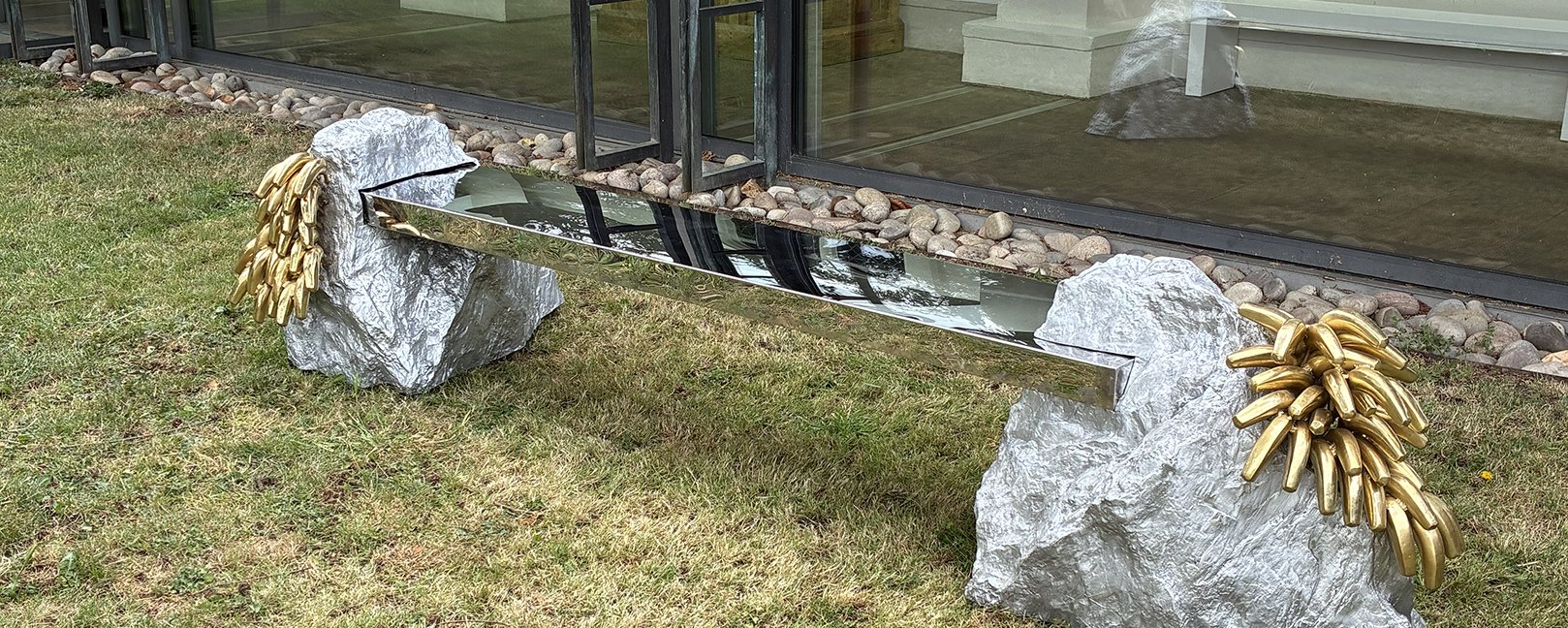 A metal bench with miniature metal mountain legs with golden brass bananas attached.